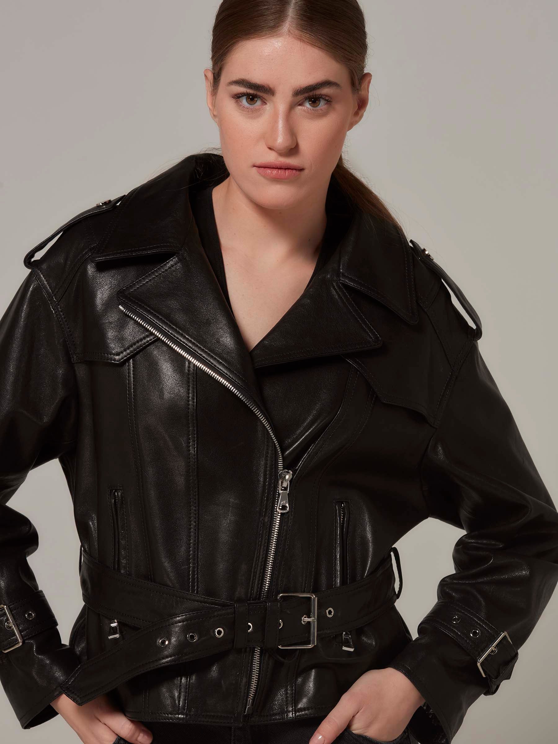 Woman in black biker leather jacket with belt, rebellious attire, motorcycle jacket, moto style, standing. (close-up)