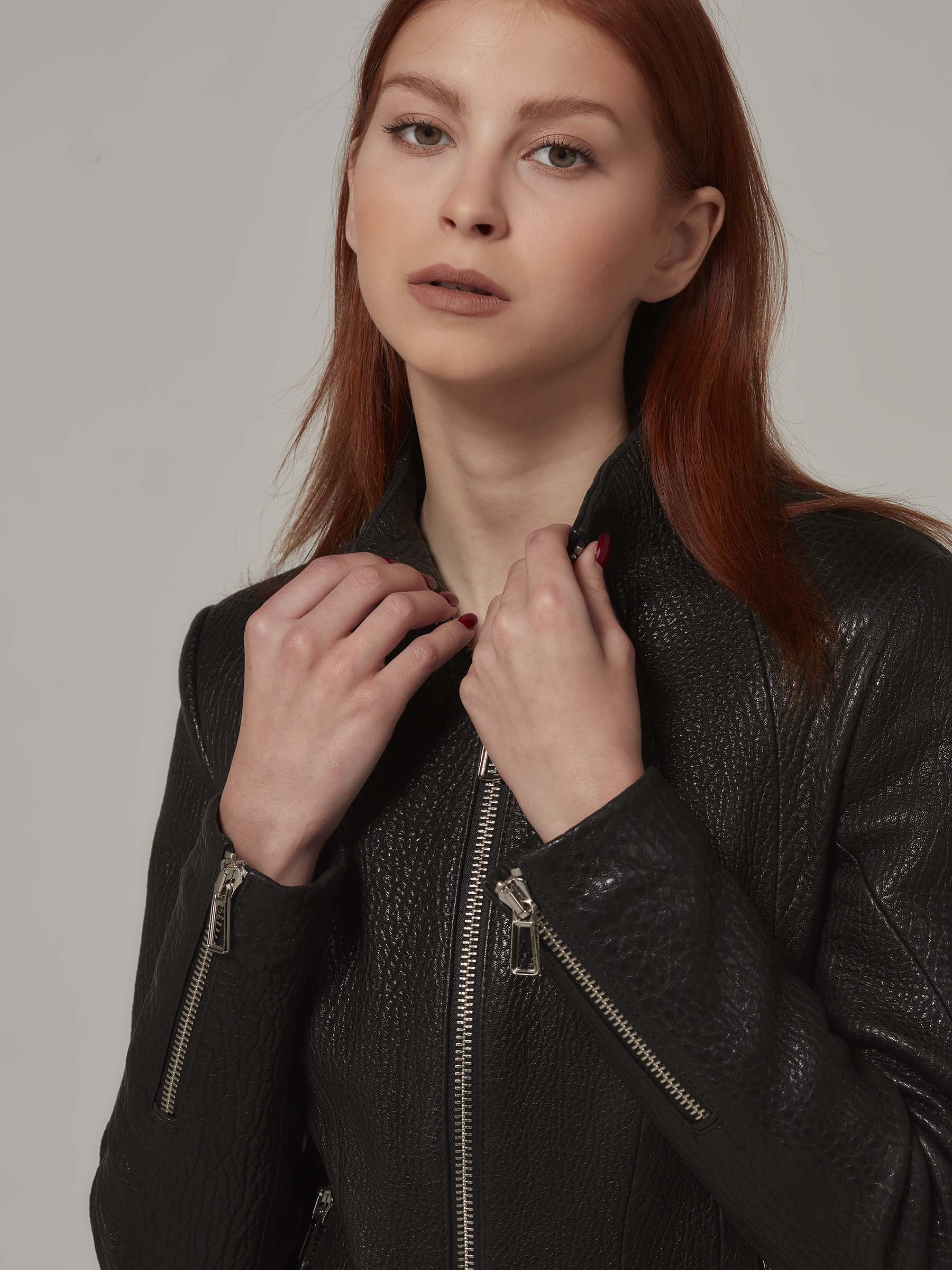 Close-up of a black leather biker jacket with a distinctive texture, worn by a woman with red hair.