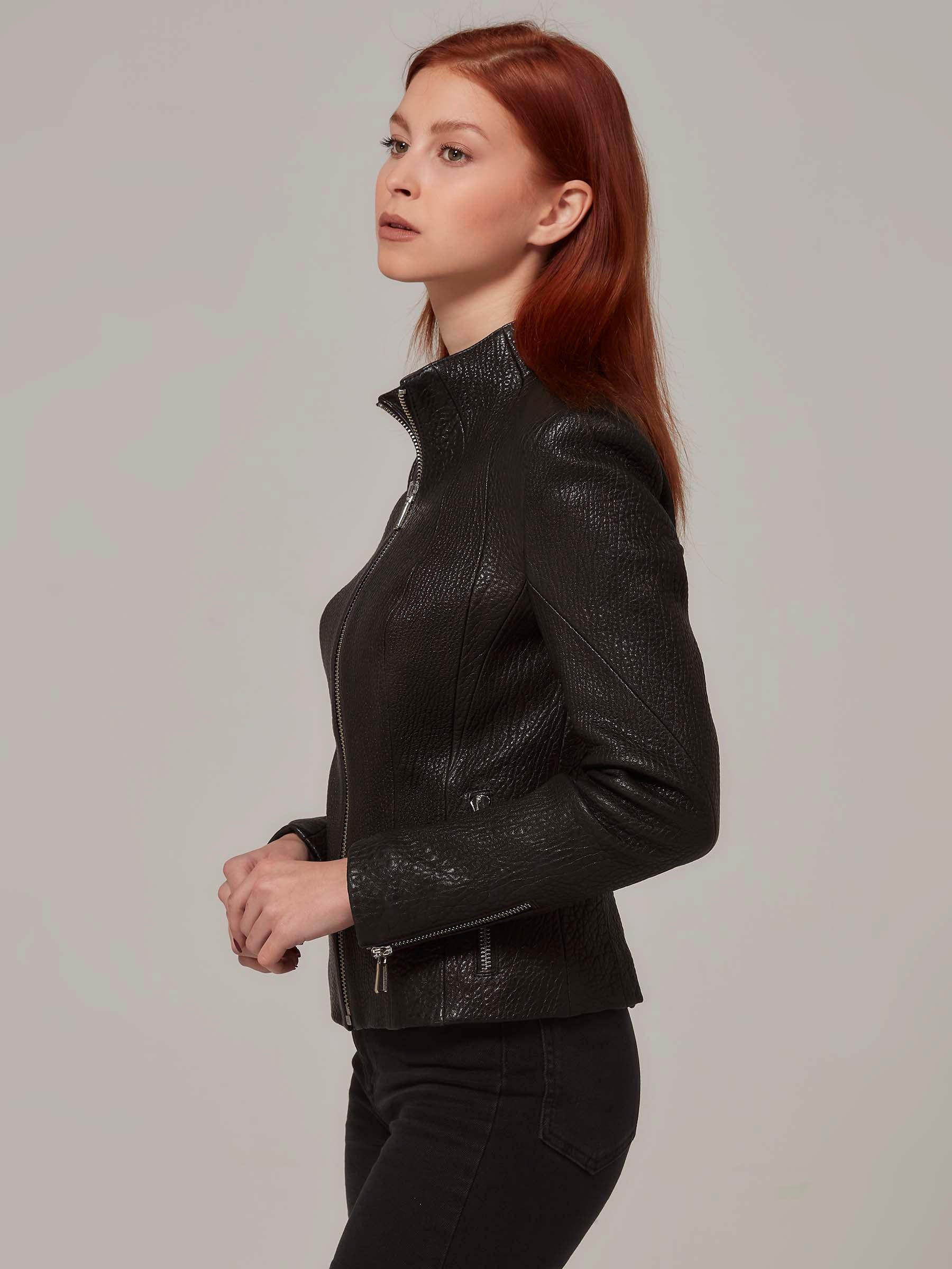 Close-up side view of a black leather biker jacket with a distinctive texture, worn by a woman with red hair.