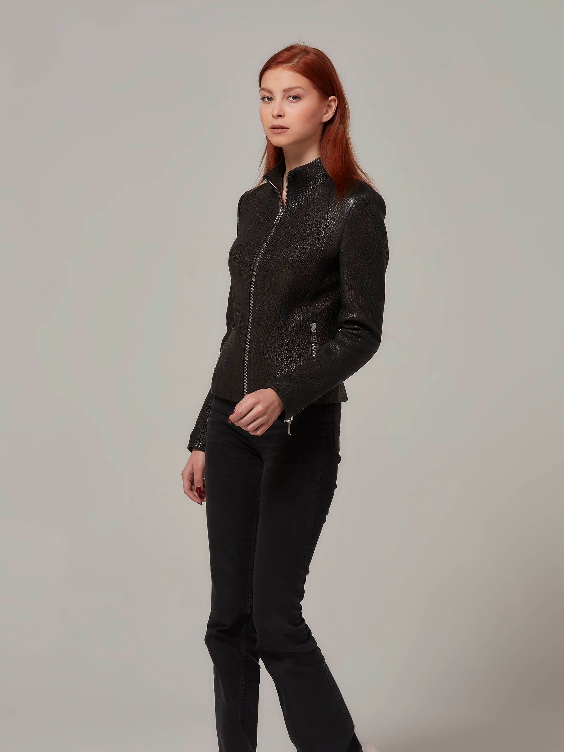 Side view of a black leather biker jacket with a distinctive texture, worn by a woman with red hair.