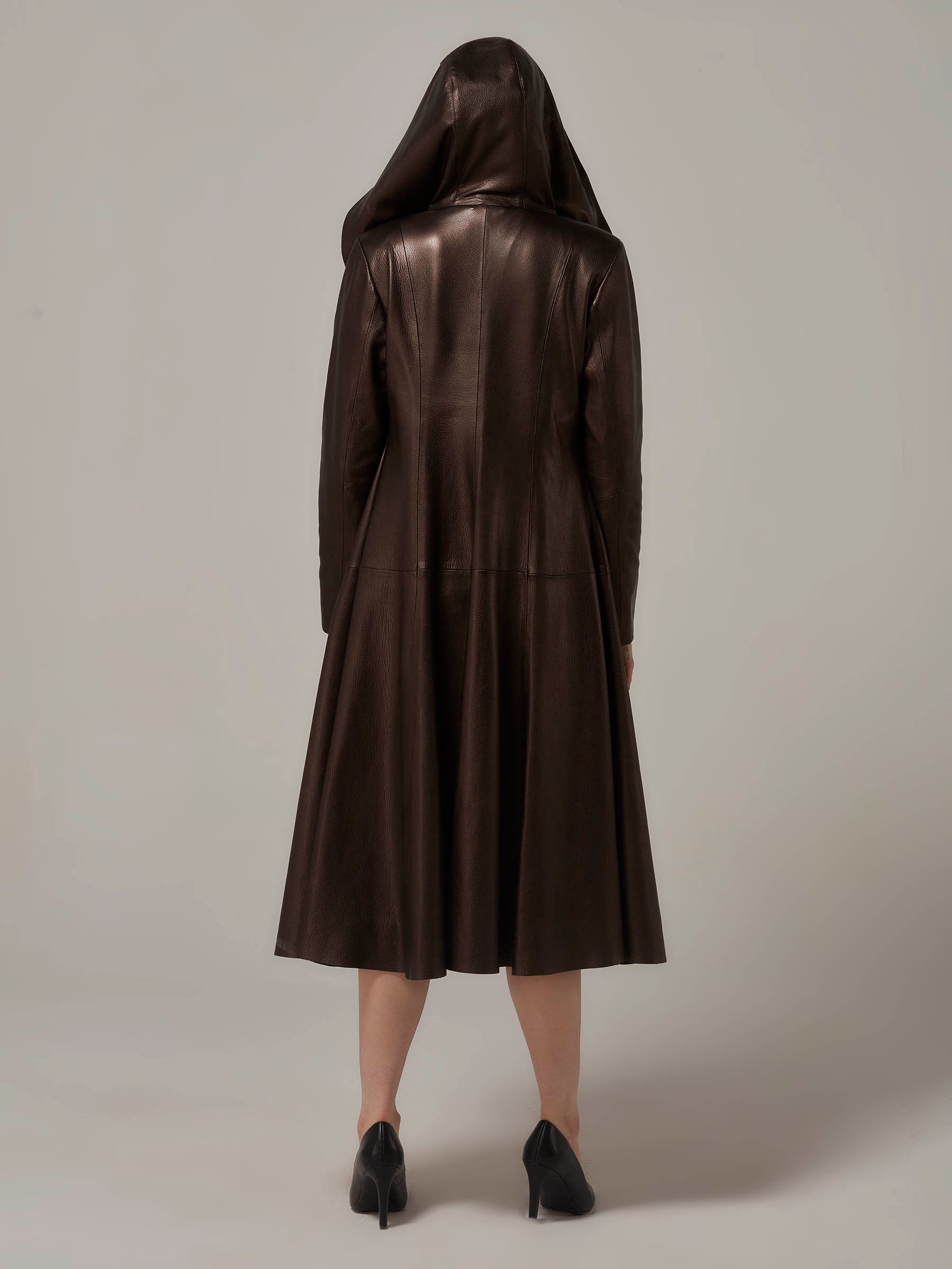 A beautiful chic woman in a black dress and leather coat, captured in a full-length photo. She is donning a fashionable dark bronze color lambskin hooded leather coat with the hood up, confidently posing in a backview.