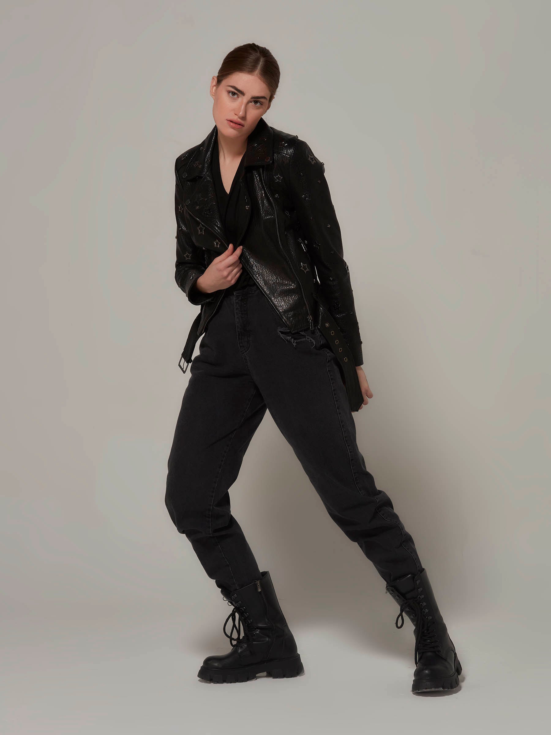 Woman in a black, biker jacket adorned with star details, with the unique texture of the leather and embodying a rebellious rock attitude.Full length standing front view fashion pose.