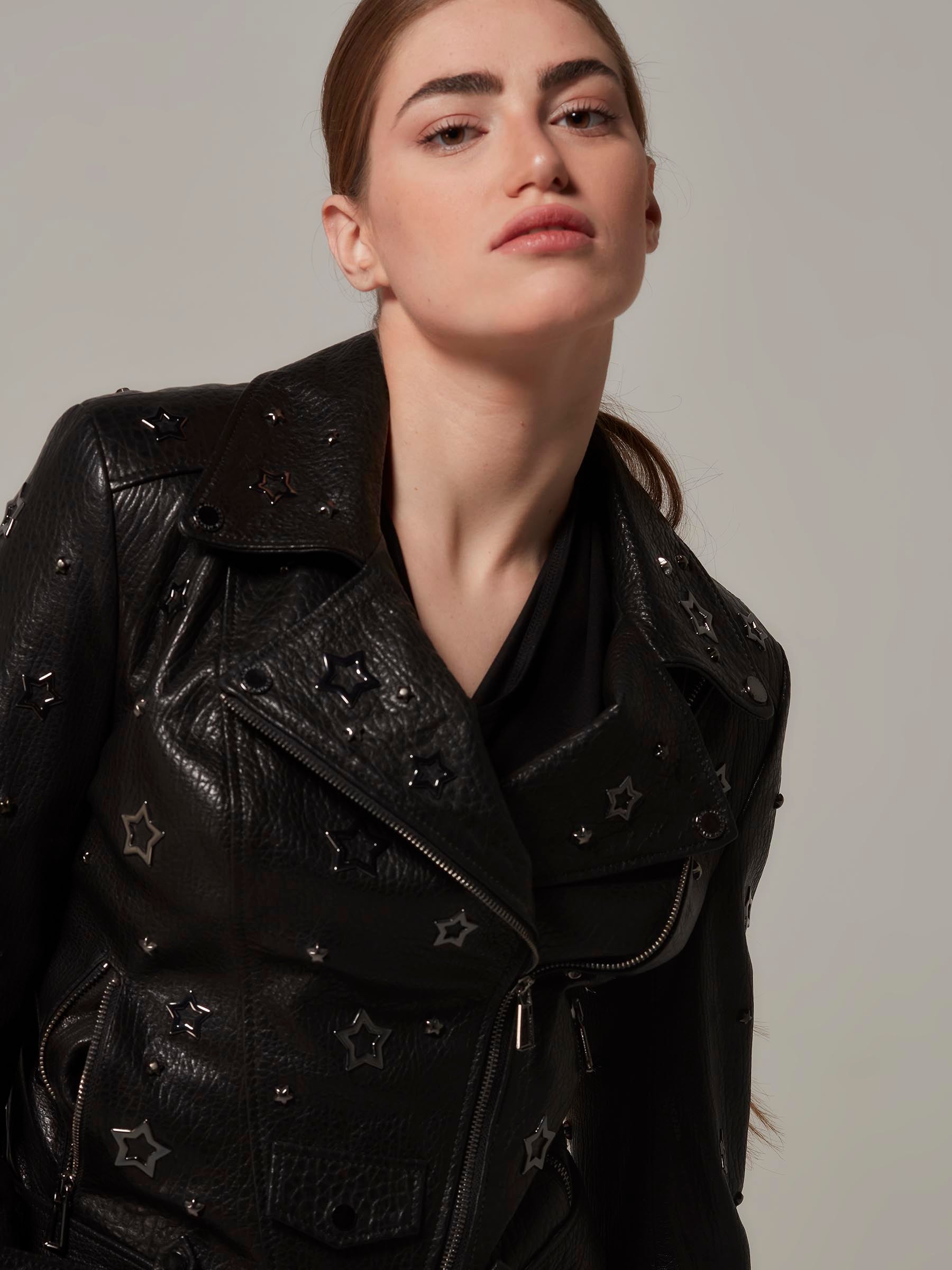 Woman in a black,  biker jacket adorned with star details, with the unique texture of the leather and embodying a rebellious rock attitude. Standing side view fashion posing. Motorcycle jacket. Close up.