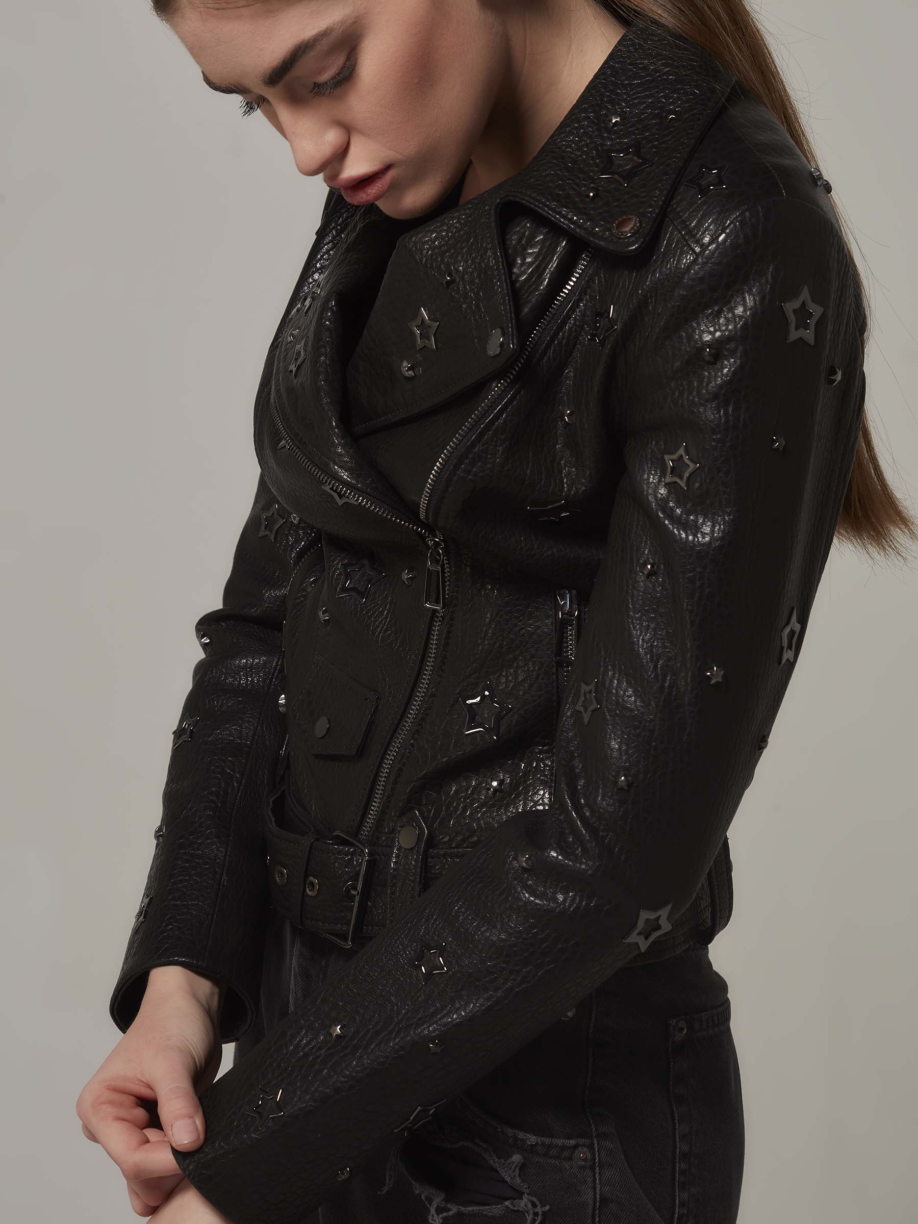 Woman in a black, biker jacket adorned with star details, with the unique texture of the leather and embodying a rebellious rock attitude. Standing front view close up pose.