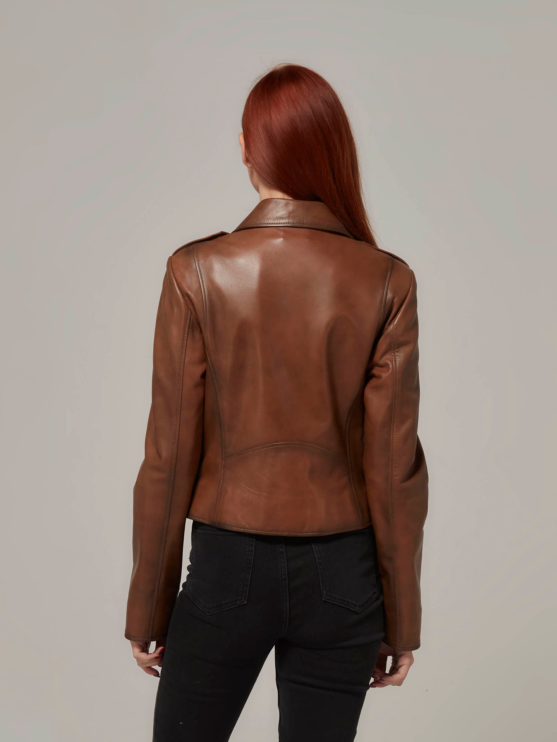 Woman in vintage brown leather biker jacket, motorcycle jacket, moto style, standing. (back view)