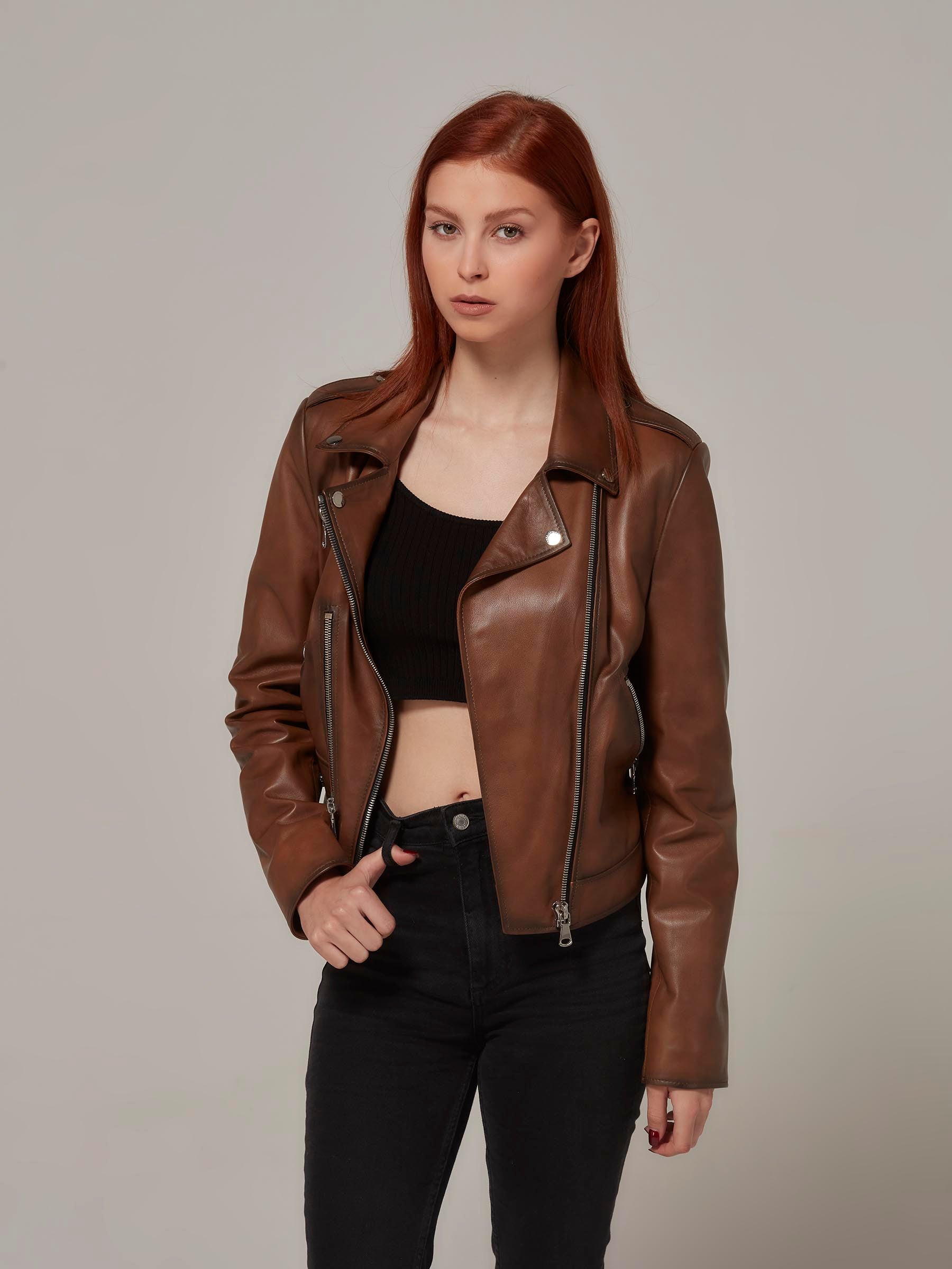 Woman in vintage brown leather biker jacket, motorcycle jacket, moto style, open front revealing, standing.