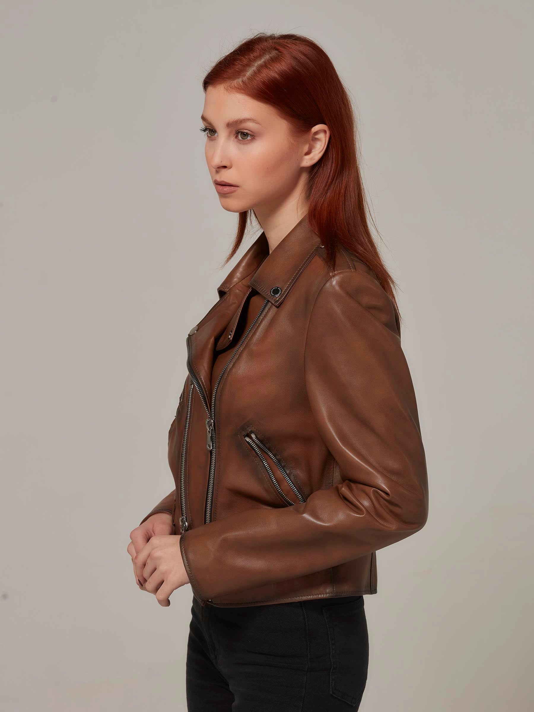 Woman in vintage brown leather biker jacket, motorcycle jacket, moto style, standing. (side view)